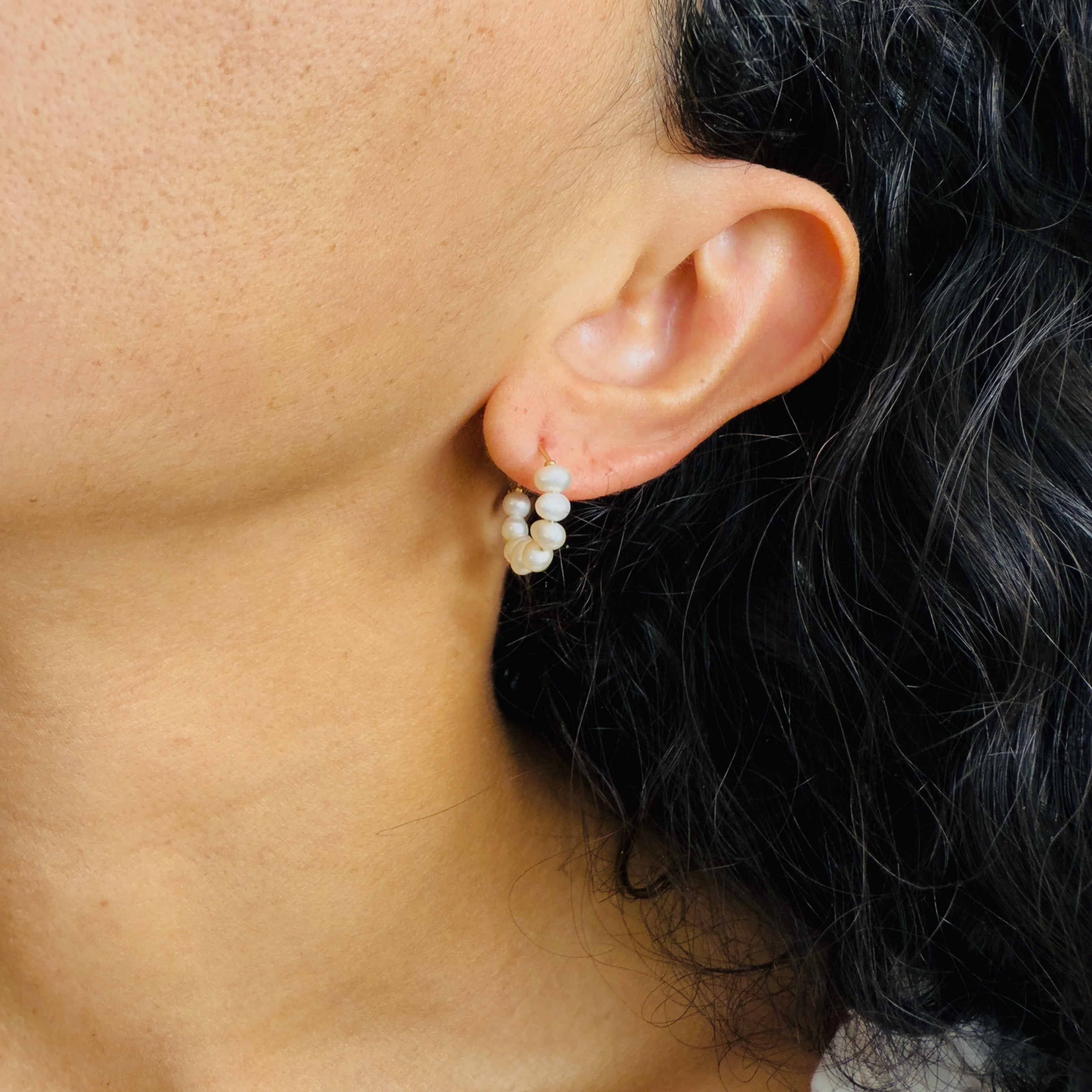 Close-up of an ear wearing a pearl earring with dark hair and skin.