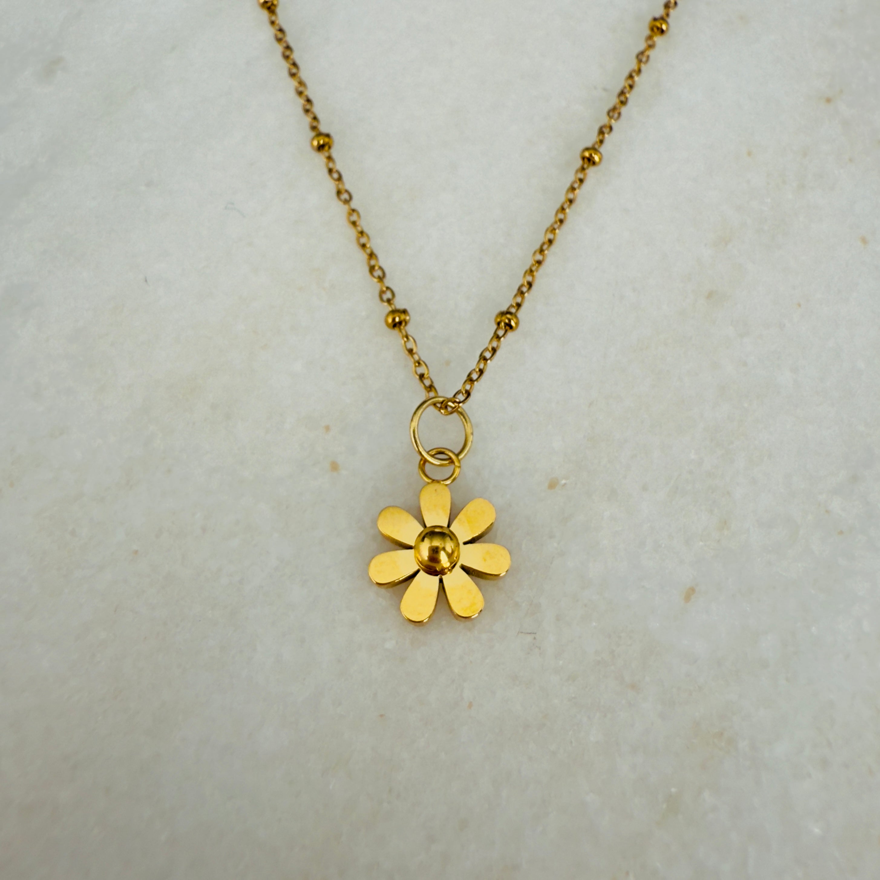 Gold flower pendant necklace on a light gray background