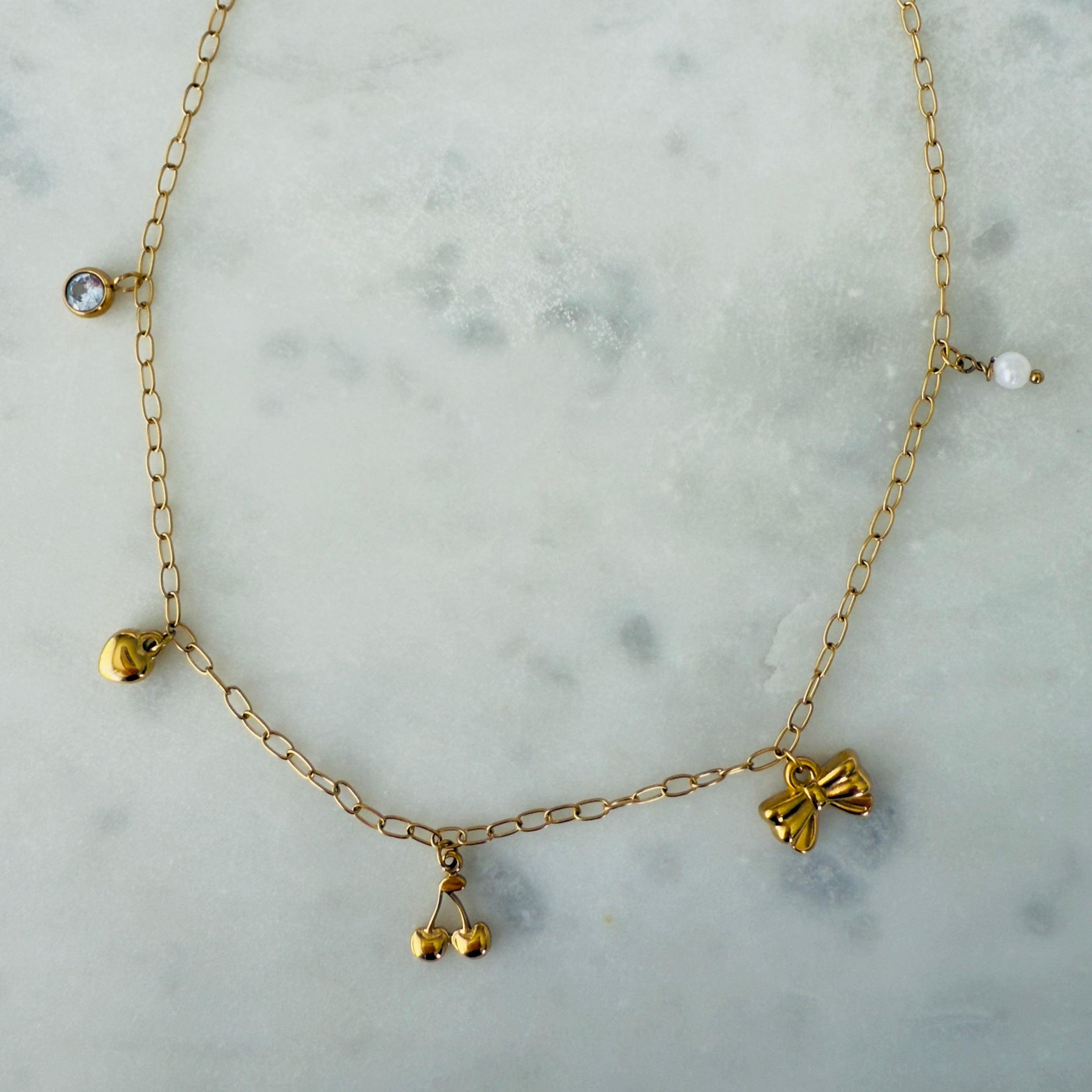 Gold charm necklace made of stainless steel with a zirconia, heart, cherries, bow and pearl charms