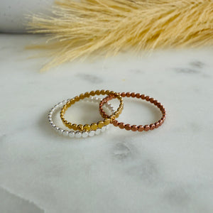 Three circles rings in silver, gold, and bronze on a marble surface with dried grass in the background.