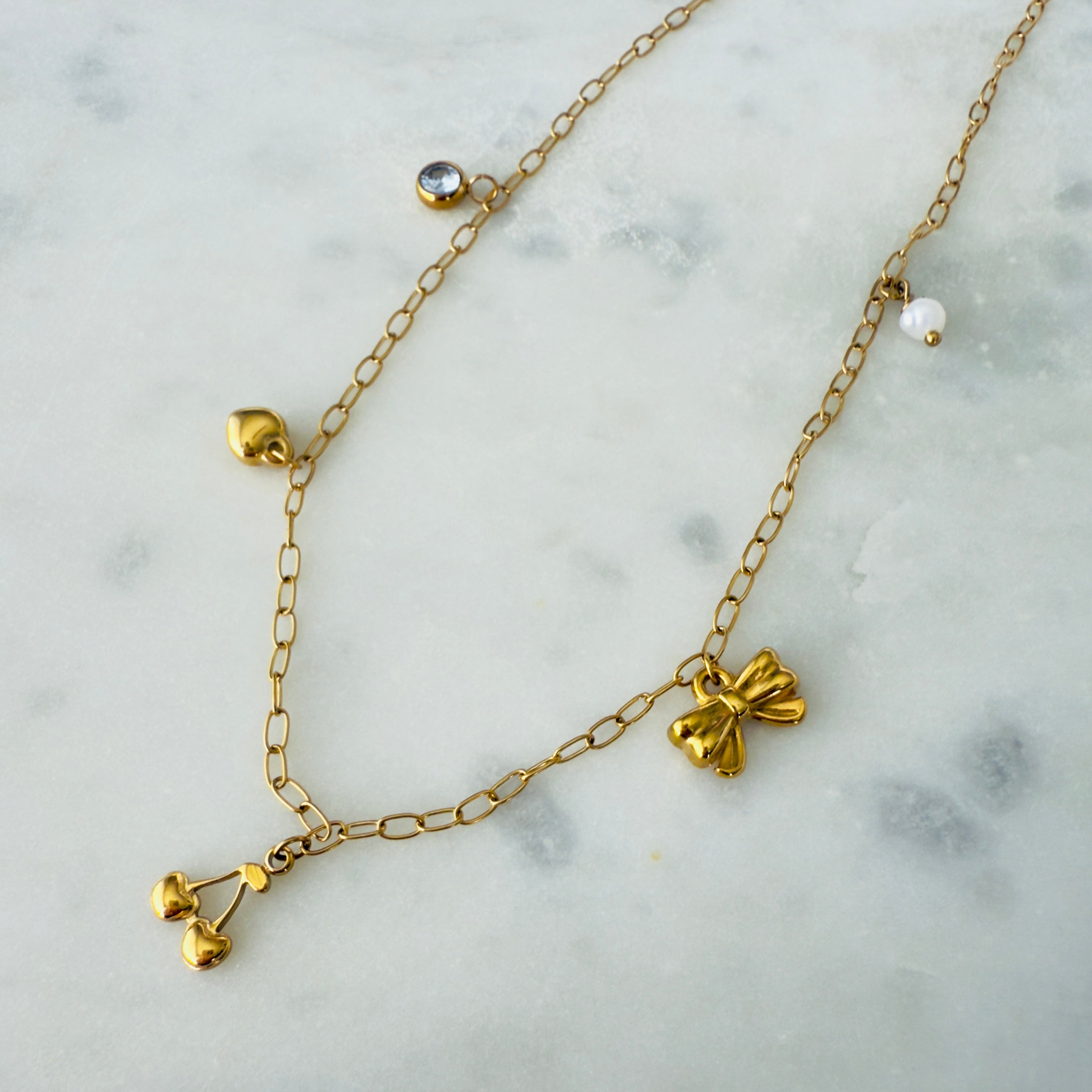 Gold charm necklace made of stainless steel with a zirconia, heart, cherries, bow and pearl charms