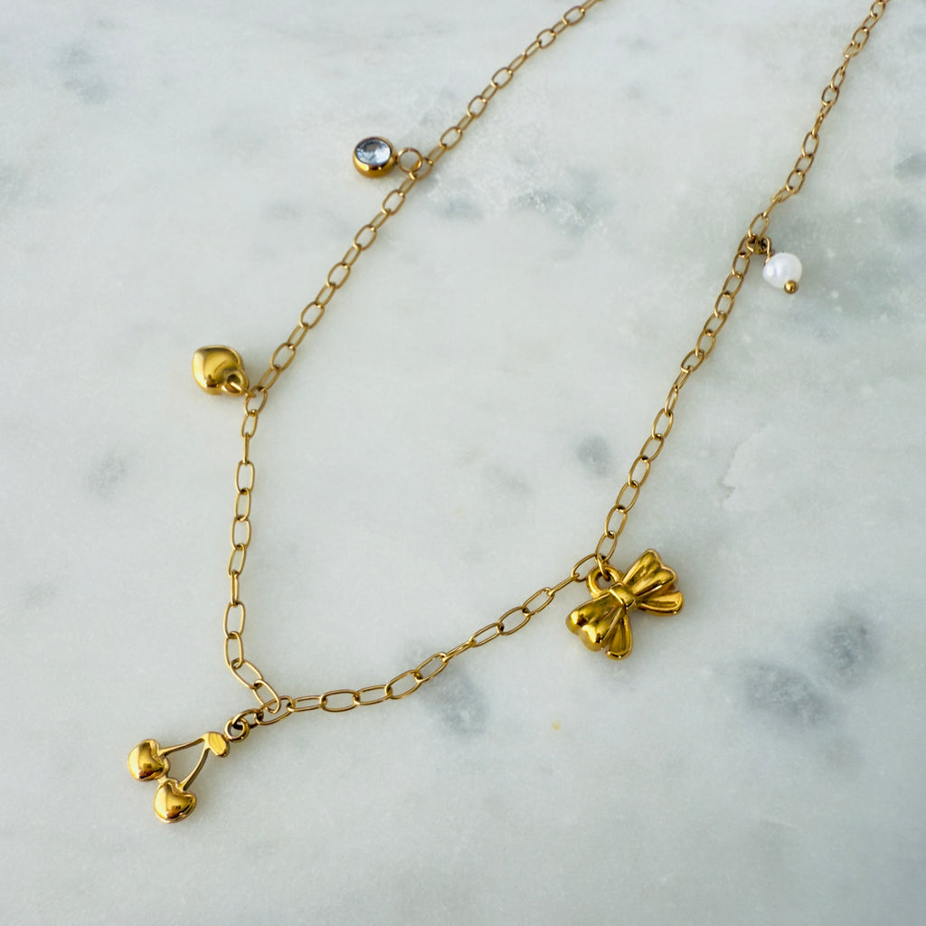 Gold charm necklace made of stainless steel with a zirconia, heart, cherries, bow and pearl charms