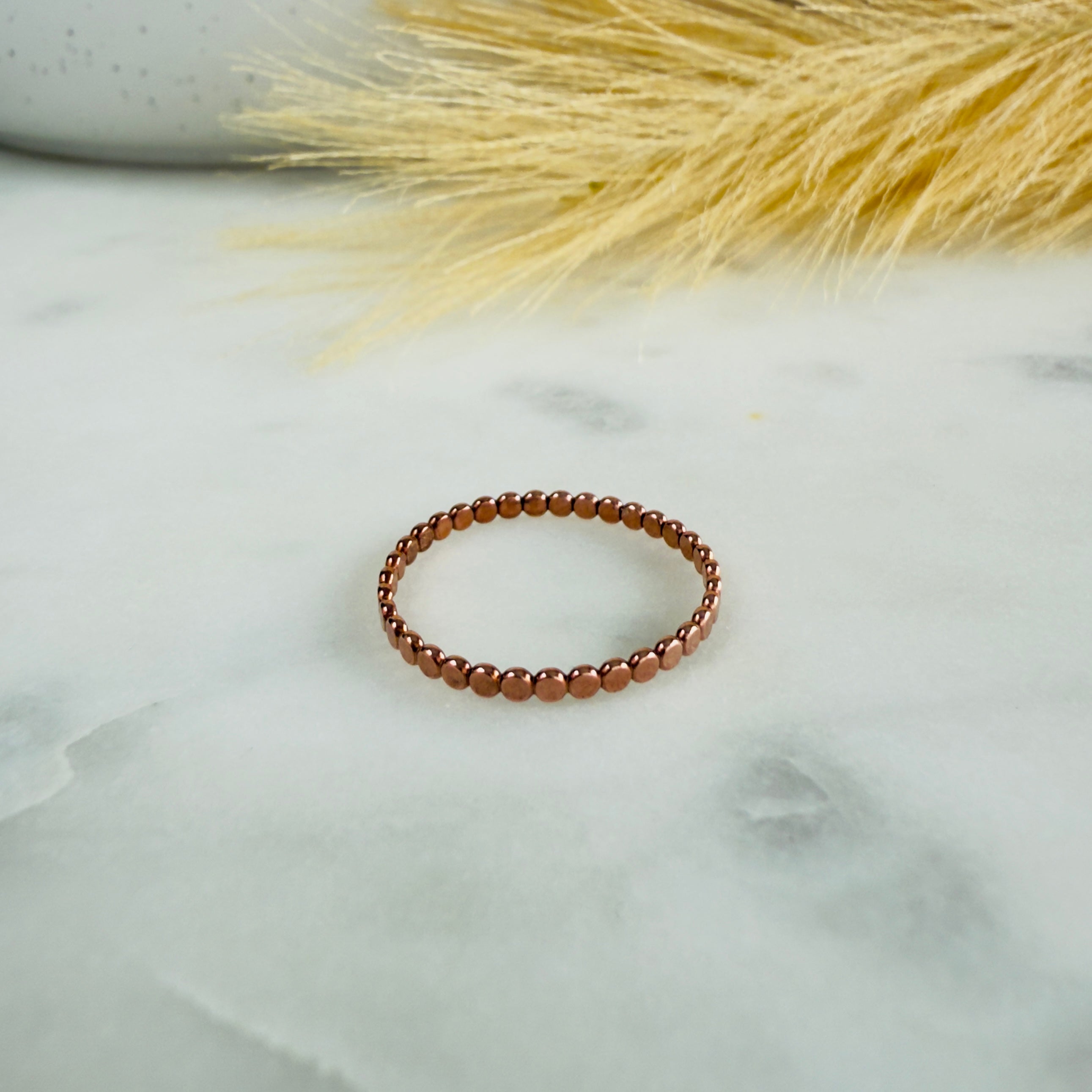 Beaded ring on a marble surface with dried grass in the background