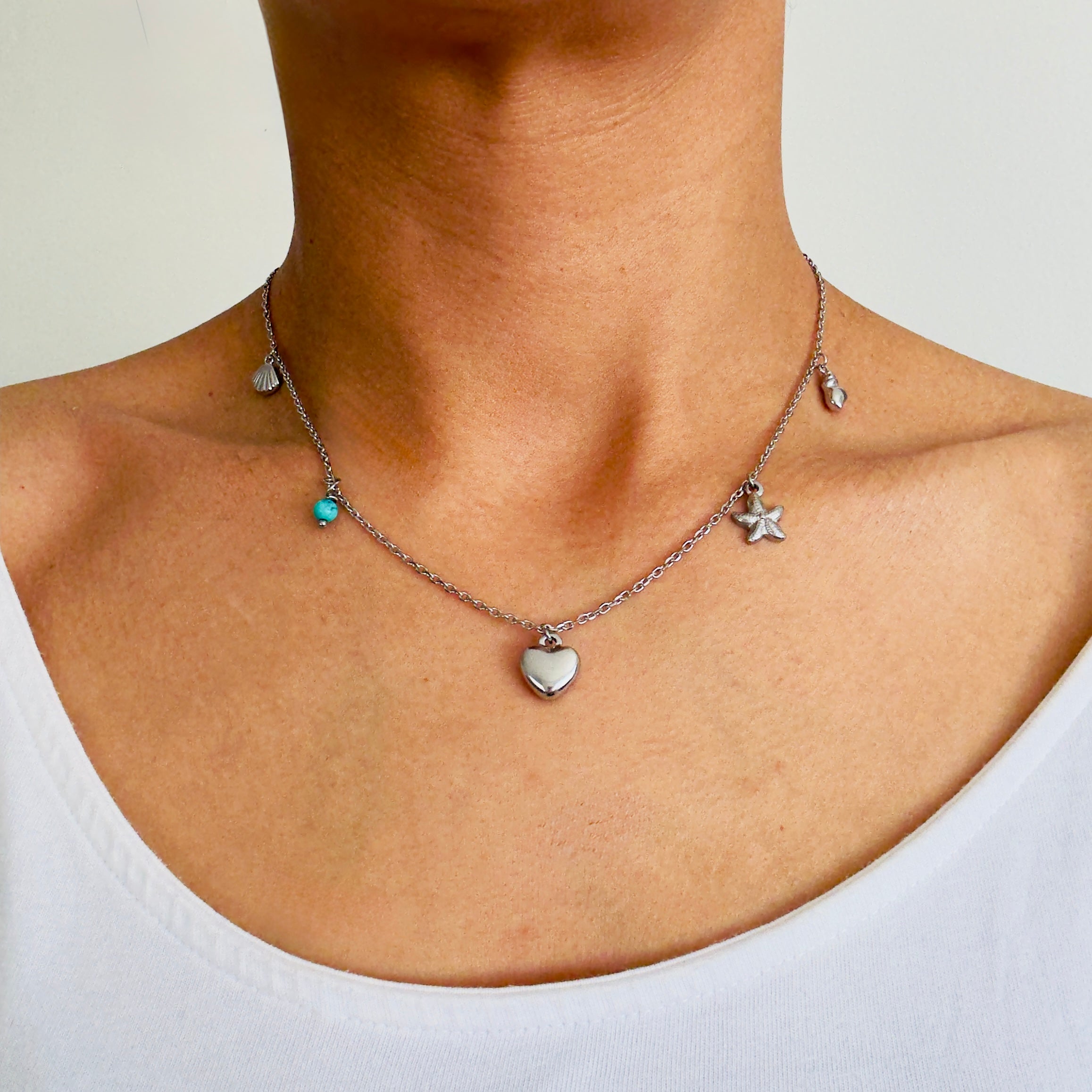 Stainless Steel charm necklace with a shell, turquoise, heart, starfish and conch charms worn by a woman