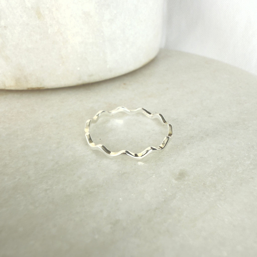 Silver ring with wavy design on a light gray surface