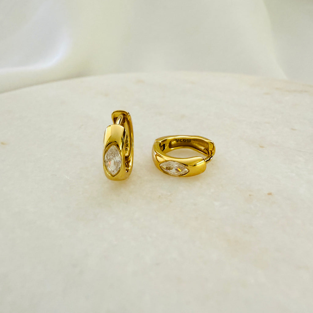 A pair of gold-colored hoop earrings with cubic zirconia stones, displayed on a white surface.