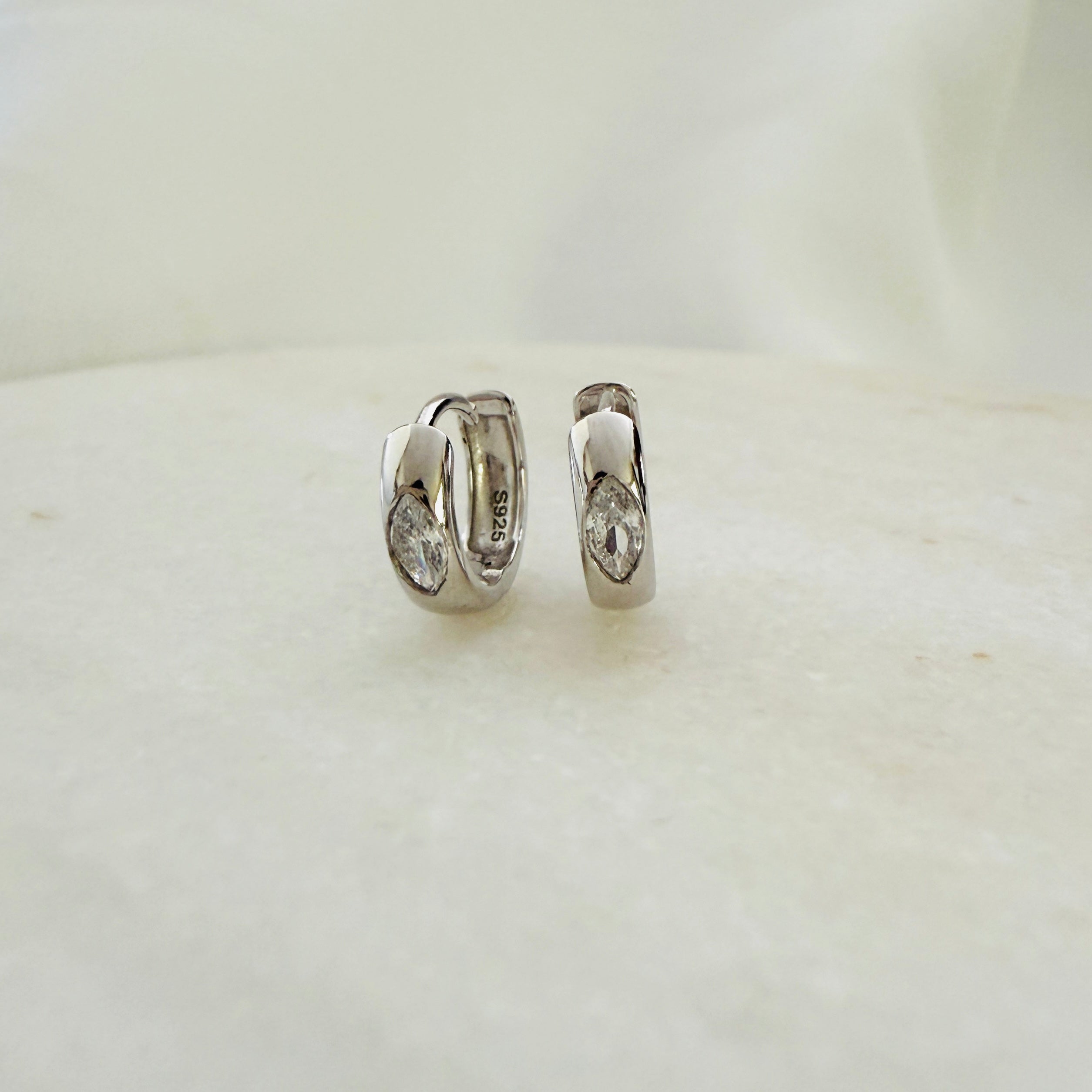 A pair of silver hoop earrings with cubic zirconia stones, displayed on a white surface.