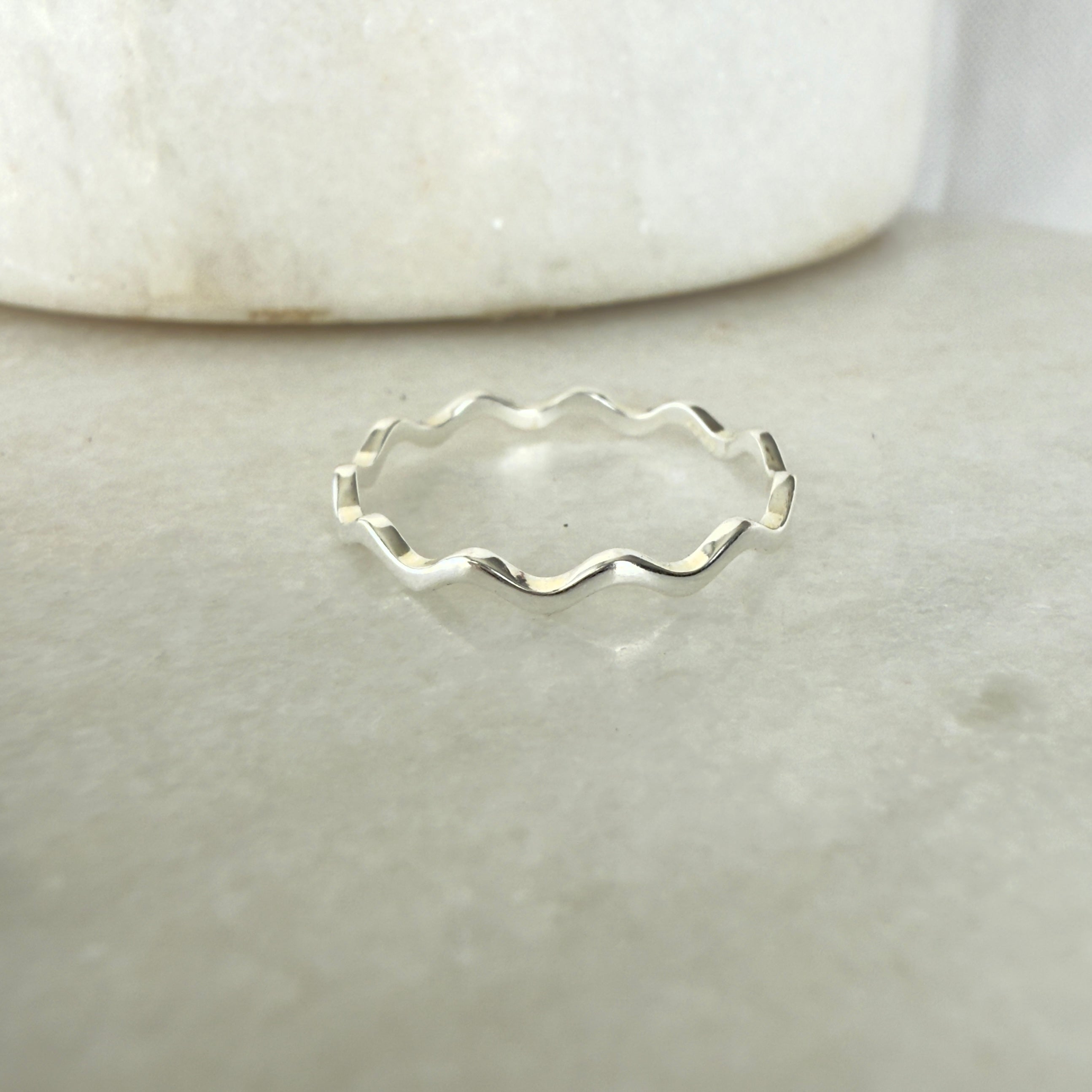 Silver ring with wavy design on a light gray background