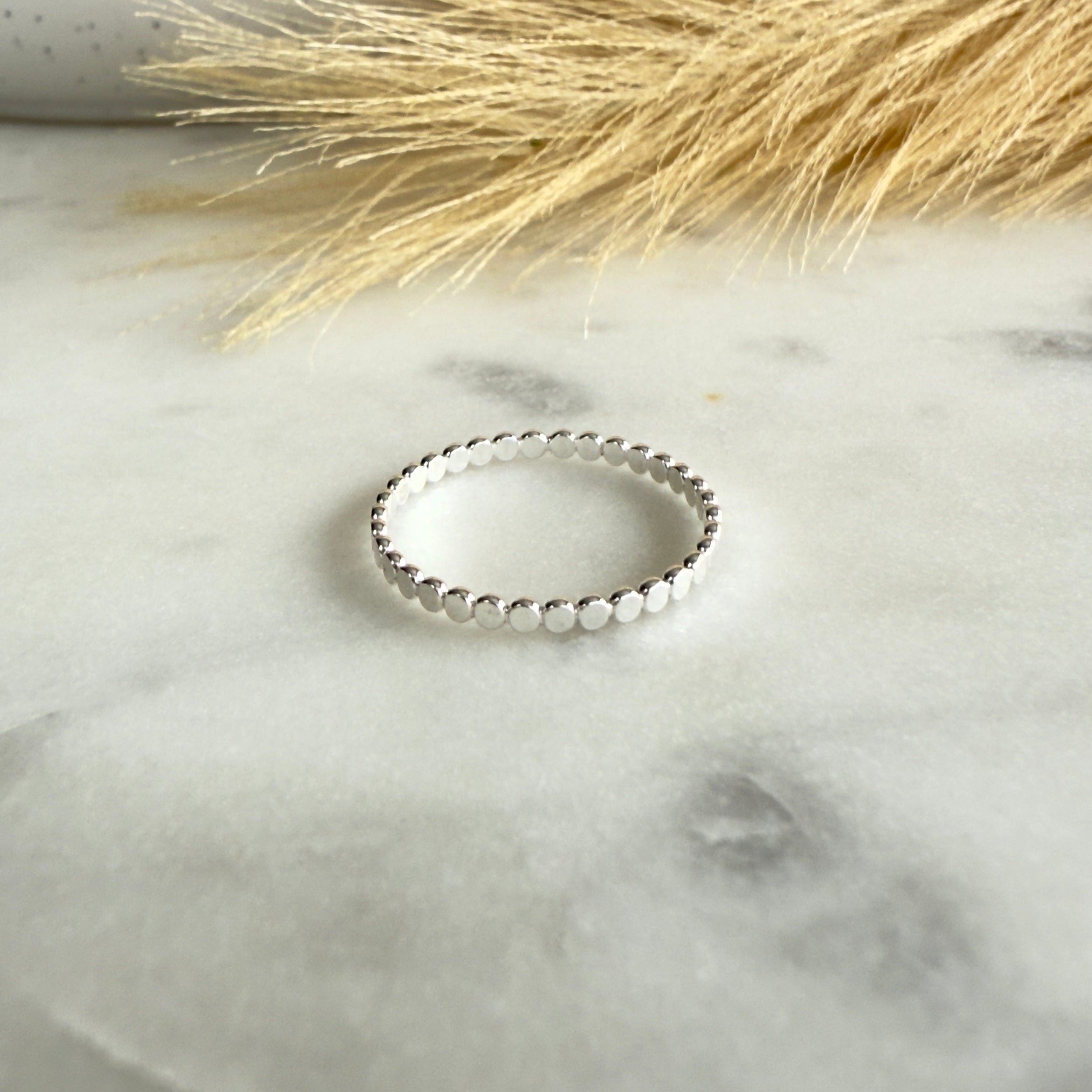 Silver beaded ring on a marble surface with dried grass in the background