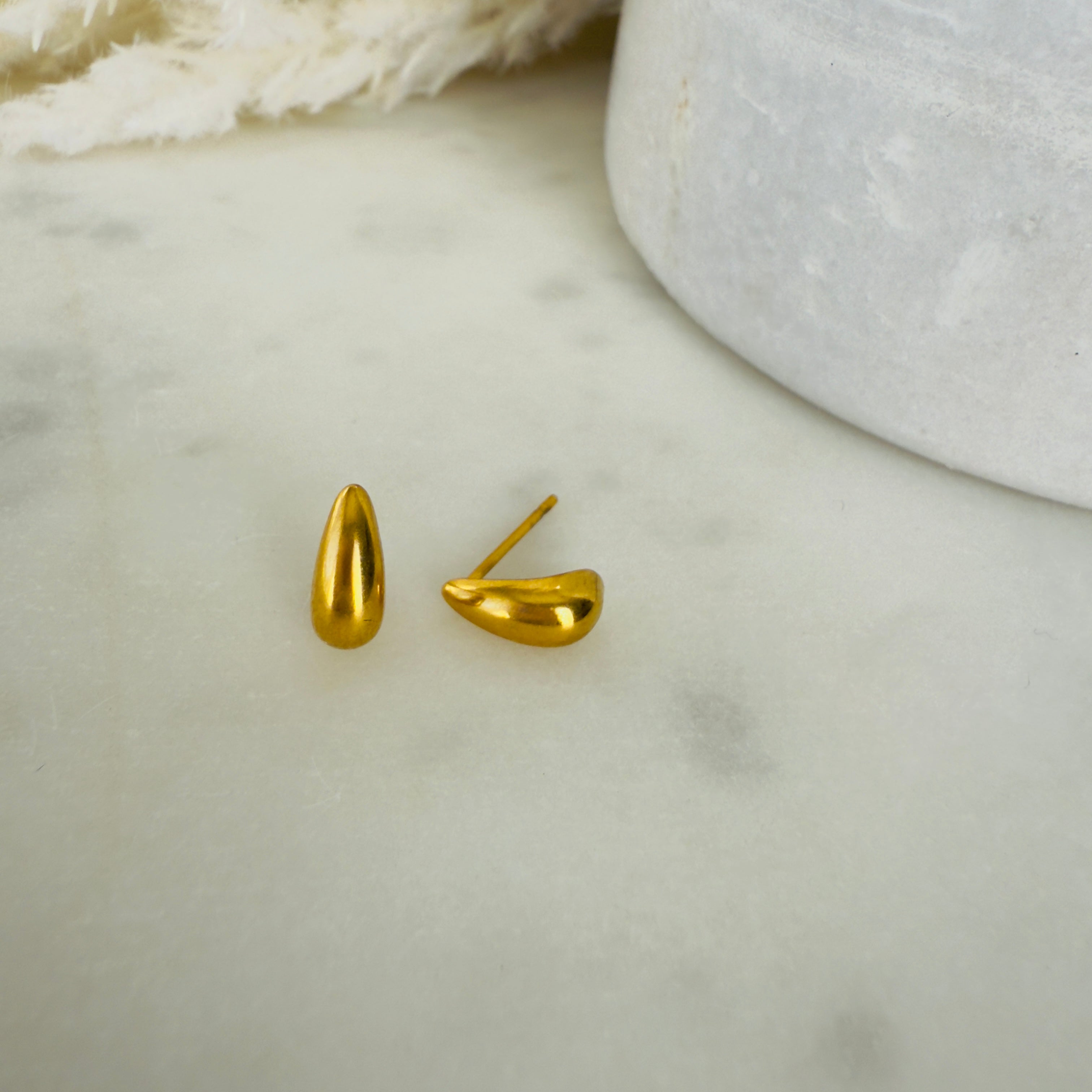 Gold teardrop earrings on a marble surface