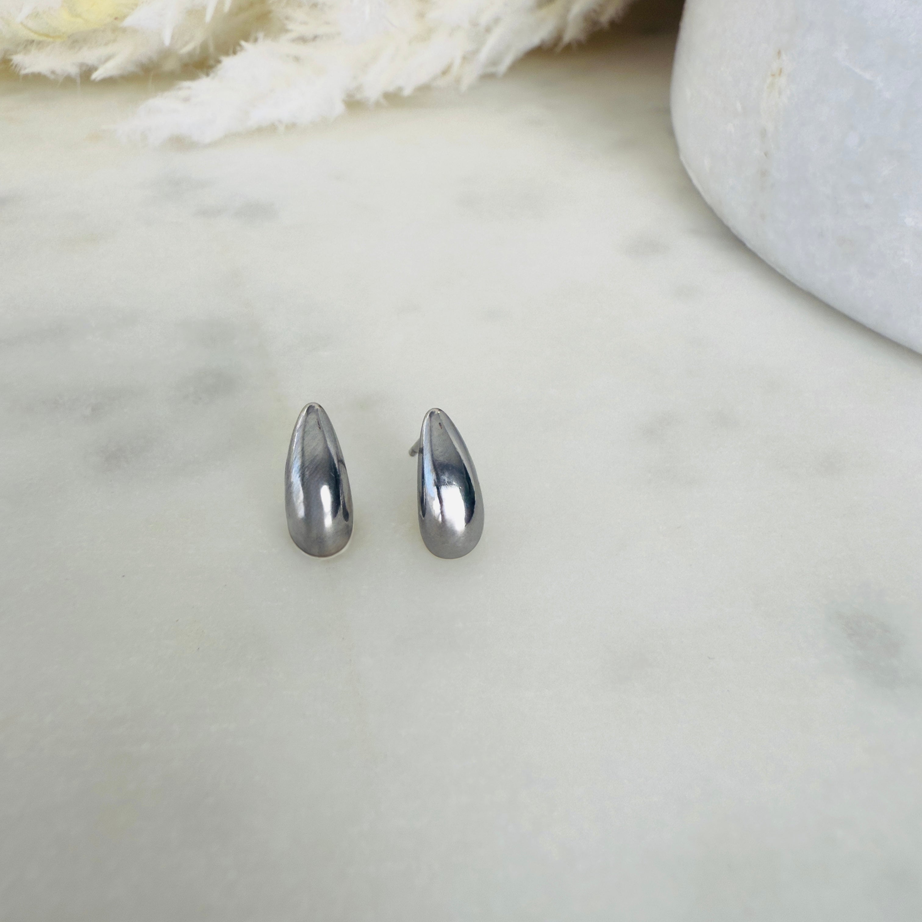 Silver teardrop stud earrings on a white  surface