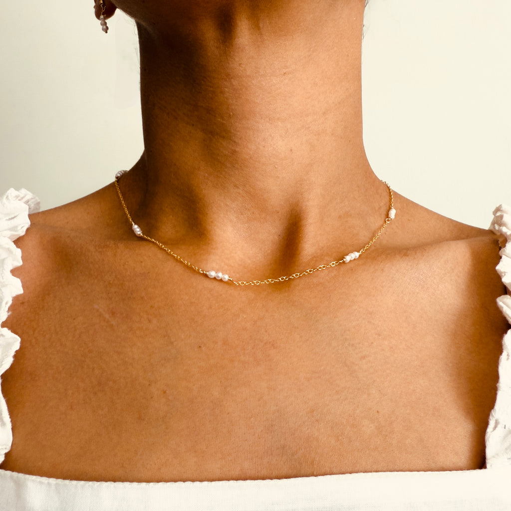 Close-up of a woman wearing a gold filled trio pearl necklace, featuring groups of  three dainty freshwater pearls evenly spaced along a fine gold chain